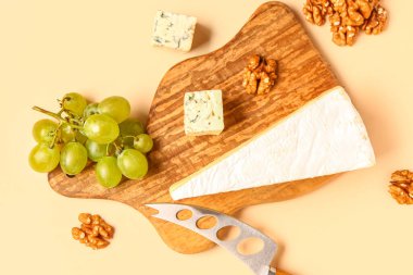 Lezzetli peynirli ahşap tahta, bej arka planda üzüm ve fındık.