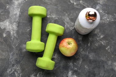 Dambıllar, su şişesi ve siyah arka planda elma.