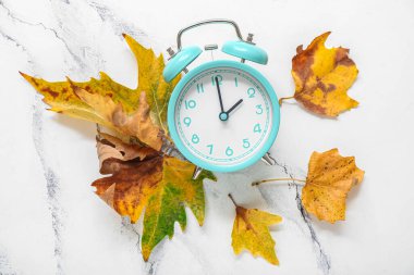 Alarm saati ve sonbahar yaprakları beyaz mermer zemin üzerinde, düz yatıyordu