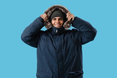 Mavi arka planda, sıcak parkalı genç adam.