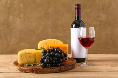 Kahverengi duvarın yanındaki masada lezzetli peynir, üzüm, şişe ve şarap tabağı.