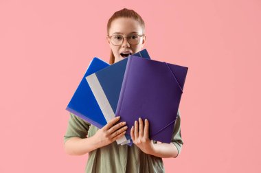 Pembe arka planda doküman klasörleri olan şaşırmış genç bir kadın.