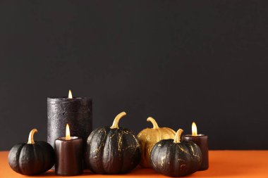 Siyah duvarın yanındaki turuncu masada mumlarla boyanmış balkabakları.