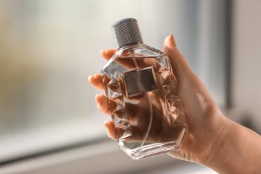 Pencerenin yanında zarif bir parfüm şişesi olan bir kadın eli.