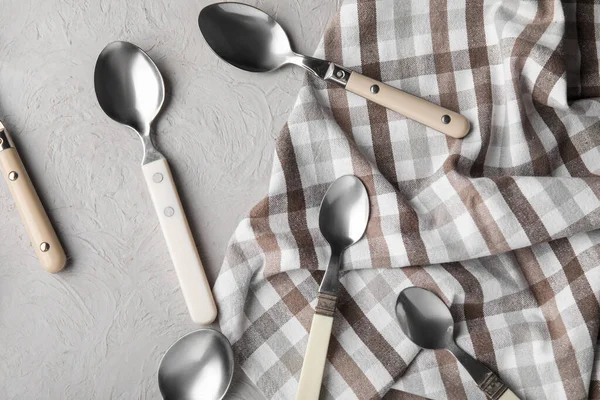 Different silver spoons and napkin on grey background