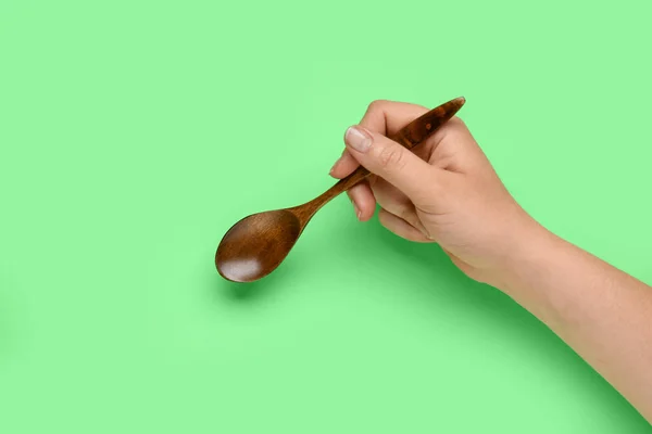 Female hand with wooden spoon on green background