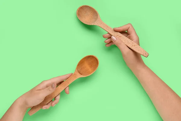 Female hands with wooden spoons on green background