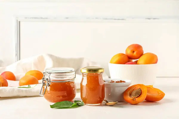 Jars with sweet apricot jam on white background
