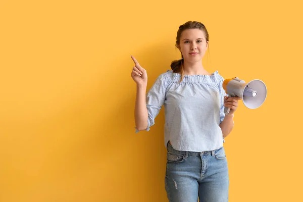 Young woman with megaphone pointing at something on yellow background