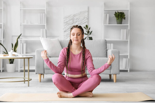 Young woman with dreadlocks meditating at home