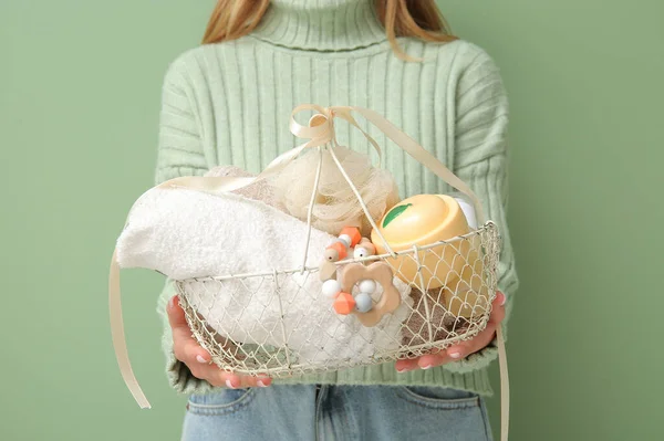 Woman with gift basket for baby on green background, closeup