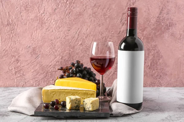 Board with tasty cheese, grapes, bottle and glass of wine on grey background