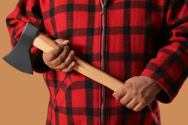 Man in red plaid shirt holding axe on beige background