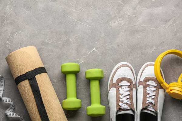 Dumbbells, shoes, headphones, yoga mat and measuring tape on grey background