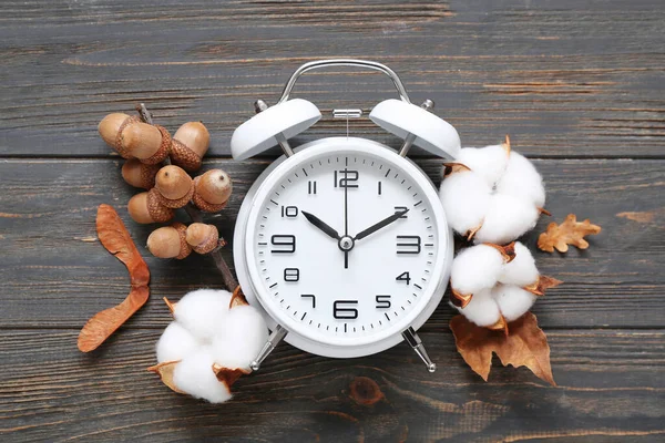 Alarm clock with cotton flowers and acorns on black wooden background