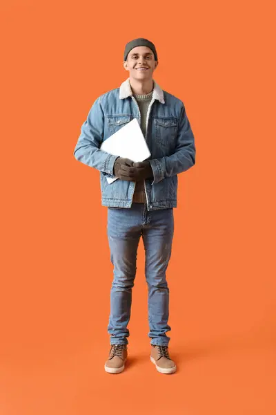オレンジ色の背景にラップトップが付いている冬の服の若者 — ストック写真