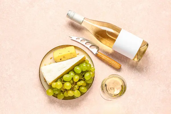 Plate with tasty cheese, grapes, bottle and glass of wine on white background