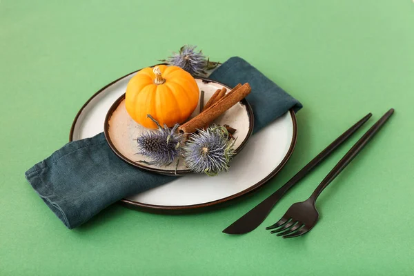 Autumn table setting with pumpkin, dried flowers and different spices on green background