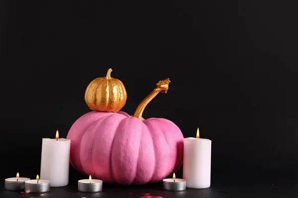Painted pumpkins and burning candles on black background
