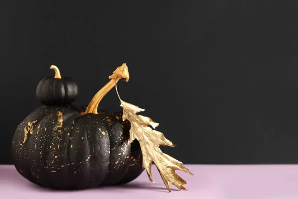 Painted pumpkins and golden leaf on purple table near black wall