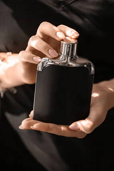 Female hands with bottle of elegant perfume near window, closeup