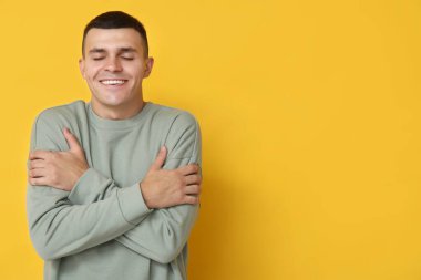 Yakışıklı genç adam sarı arka planda kendine sarılıyor.