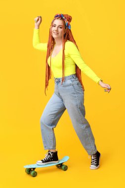 Sarı arka planda kaykay süren, rastalı genç bir kadının portresi.