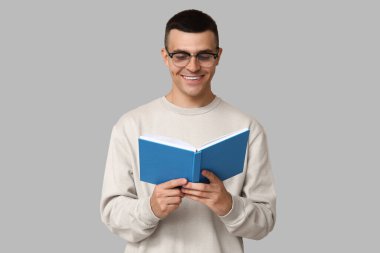 Yakışıklı genç adam gri arka plan hakkında kitap okuyor.