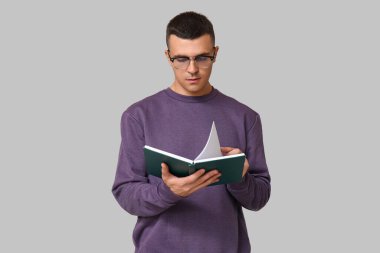 Yakışıklı genç adam gri arka plan hakkında kitap okuyor.