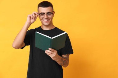 Yakışıklı genç adam sarı arka planda kitap okuyor.
