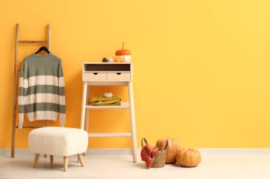 Beyaz masa, balkabağı ve kazak turuncu duvarın yanındaki merdivende asılı.