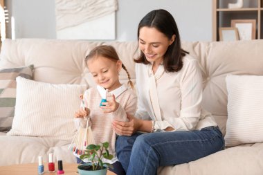 Güzel anne ve oje paletli küçük tatlı kızı evdeki kanepede oturuyorlar.