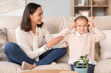Güzel anne ve tatlı lolipopları olan tatlı küçük kızı evdeki kanepede oturuyorlar.