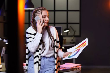 Renk paletleri olan kadın tasarımcı gece ofiste cep telefonuyla konuşuyor.