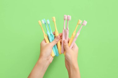 Yeşil arka planda renkli plastik diş fırçaları olan kadın elleri.