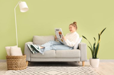 Young woman reading newspaper on sofa at home