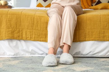 Yatak odasında dinlenen yumuşak terlikli genç bir kadın.