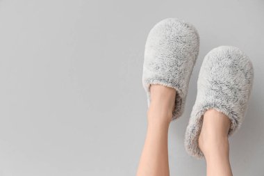 Gri arka planda yumuşak terlikler giymiş kadın bacakları.