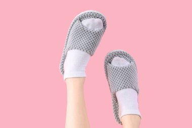 Pembe arka planda gri yumuşak terlikler giyen kadın bacakları.