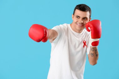 Kırmızı kurdeleli ve mavi arka planda boks eldivenli genç adam. Dünya AIDS Günü konsepti