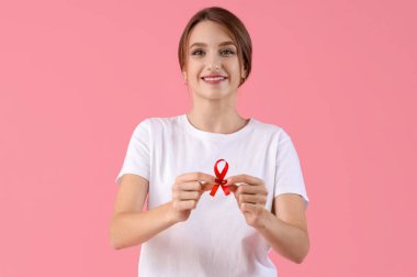 Pembe arka planda kırmızı kurdeleli güzel bir genç bayan. Dünya AIDS Günü konsepti