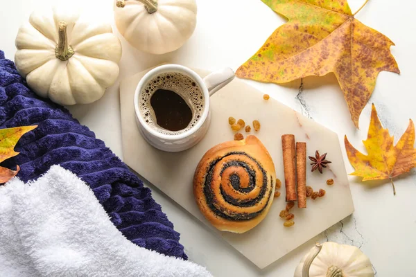 Composition with cup of aromatic coffee, bun and autumn decor on light background