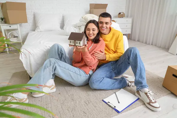 Happy young couple with house model in bedroom on moving day