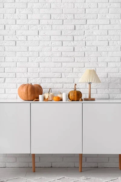 Cabinet with pumpkins, lamp and candles near white brick wall