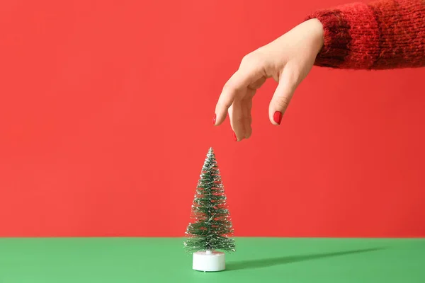 Female hand with red manicure and decorative Christmas tree on color background
