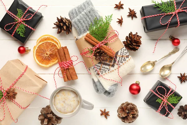 Knitted socks with Christmas gift boxes, spices and cup of coffee on white wooden background