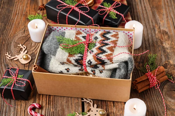 Gift box with knitted socks, burning candles and Christmas decorations on wooden background