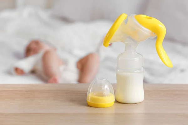 Breast pump with milk on table in bedroom, closeup