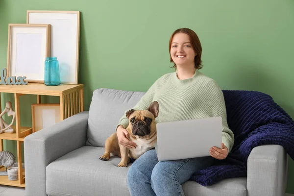 Young woman with cute dog and laptop sitting on sofa at home