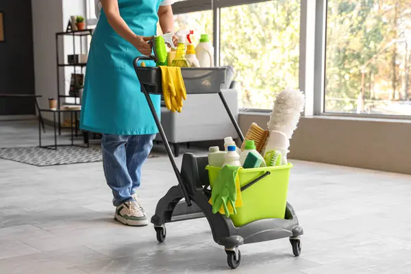 Female janitor with trolley of cleaning supplies in room
